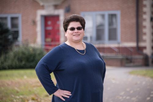 Woman wearing dark shaded glasses standing in front of Gabriel House on Muhlenberg College campus.